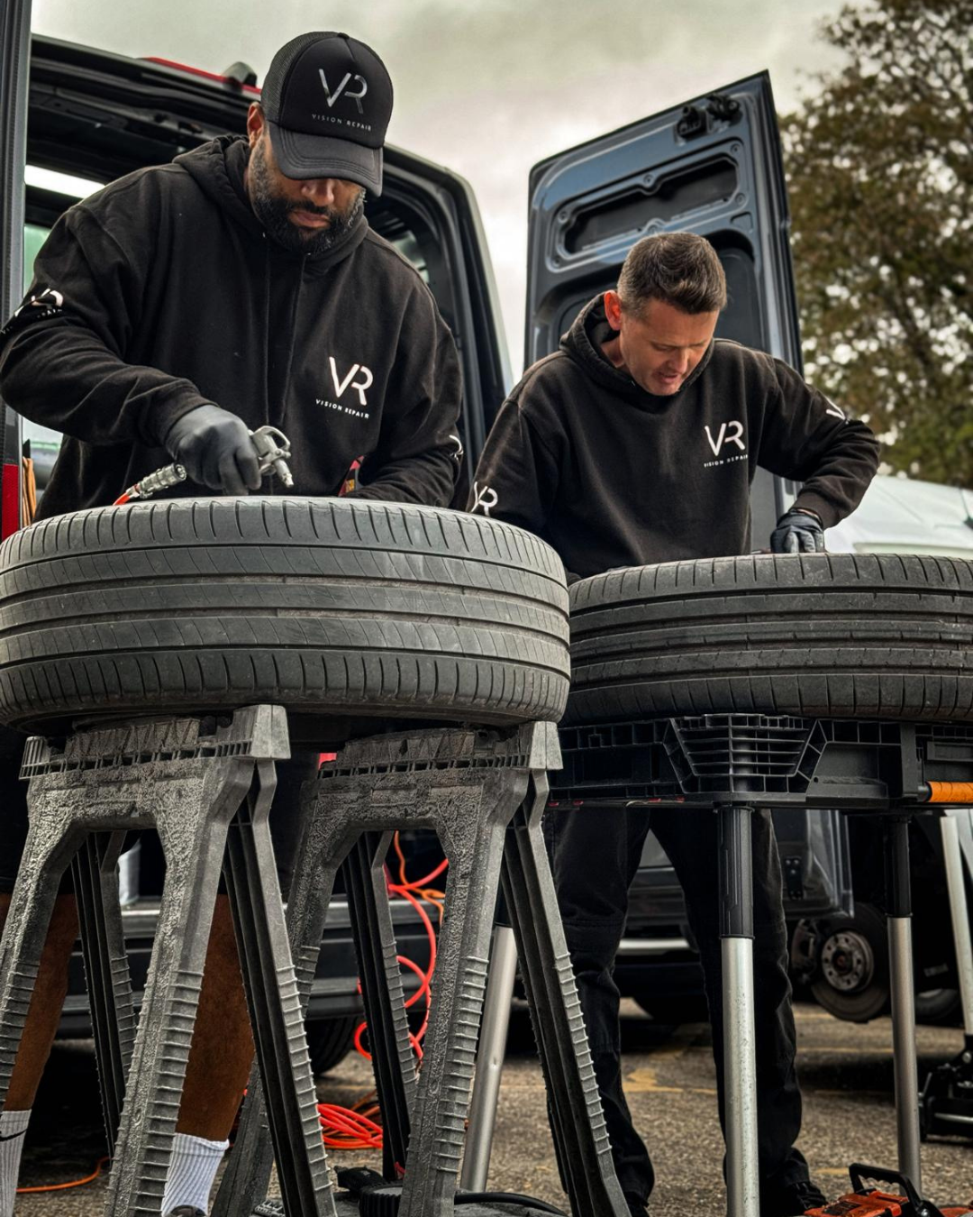 Two Vision Repair technicians working on alloy wheels at a mobile workshop
